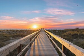 A wooden boardwalk leading to the beach with a sunset in the background.