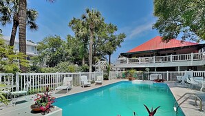 A swimming pool with a white fence, lounge chairs, and potted plants. - Tybreeza A | Apartment, Shared Pool, Near Beach! (Tybee Island)