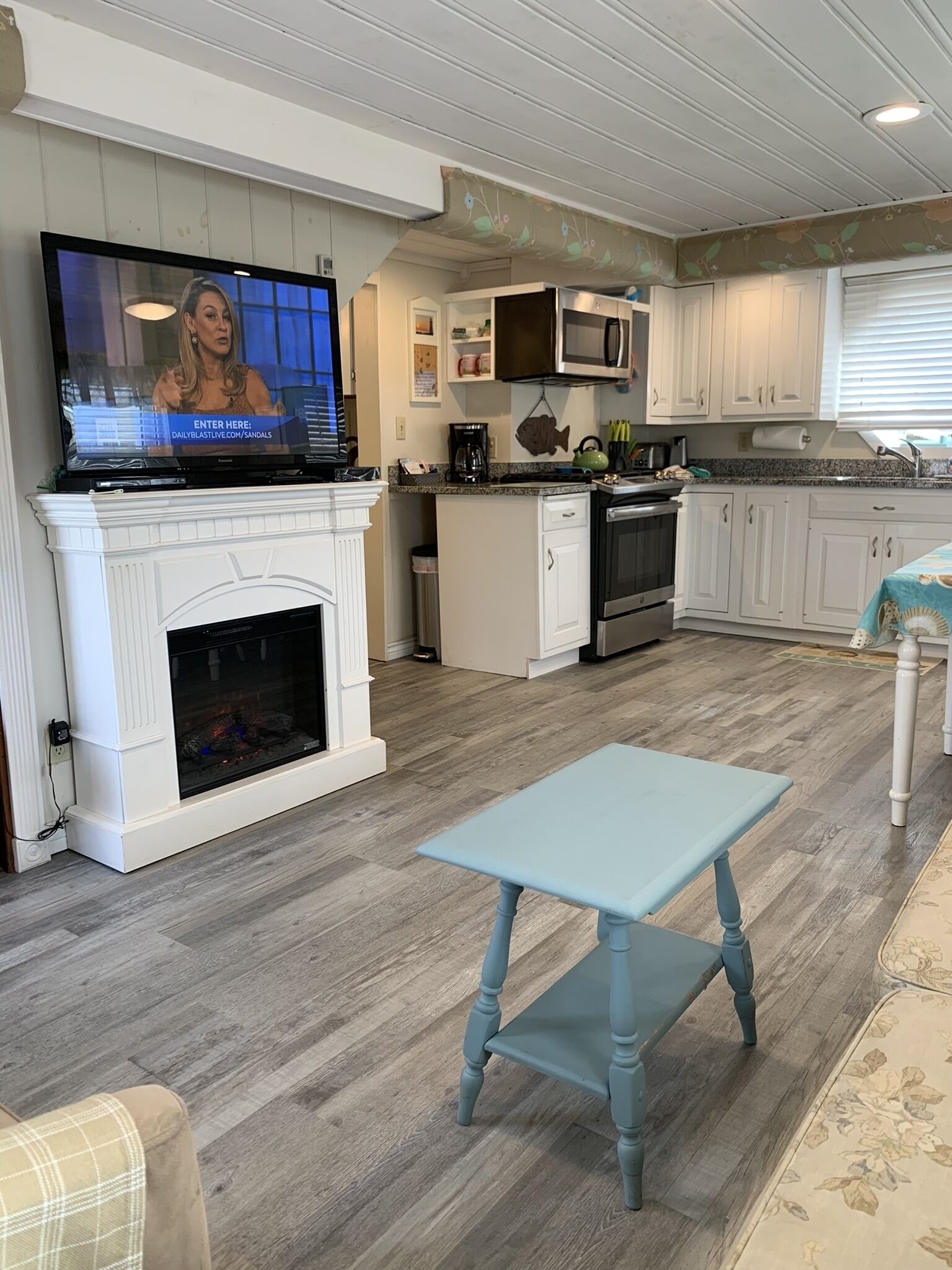 A modern kitchen with a fireplace, a dining area, and a television displaying a news program.