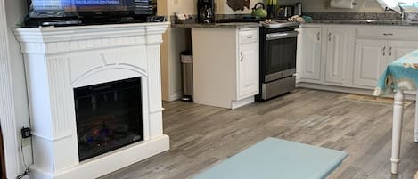A modern kitchen with a fireplace, a dining area, and a television displaying a news program.