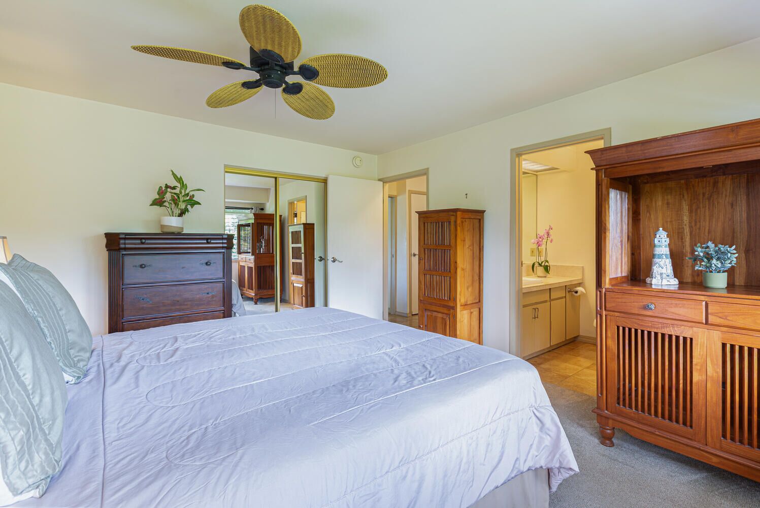 A bedroom with a bed, dresser, wardrobe, and a ceiling fan.