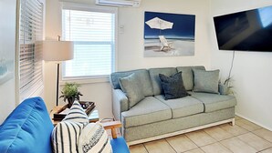 A living room with a blue sofa, a grey couch, and a flat-screen TV mounted on the wall. - Captains Quarters A | 1.5 Blocks to Beach and Pier (Tybee Island)