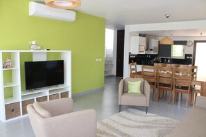 Un salon moderne doté d’un téléviseur à écran plat, d’un canapé beige et d’un coin repas avec des chaises et une table en bois.