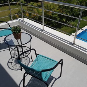 Un balcon avec deux chaises et une table, donnant sur une piscine et une végétation luxuriante.