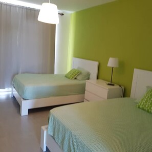 Une chambre d’hôtel avec deux lits, une table de chevet avec une lampe et une fenêtre avec des rideaux.