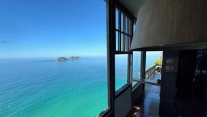 A room with a large window overlooking a turquoise sea and a small island. -  CLIFFSIDE - Boutique Hotel & Spa (Rio de Janeiro)