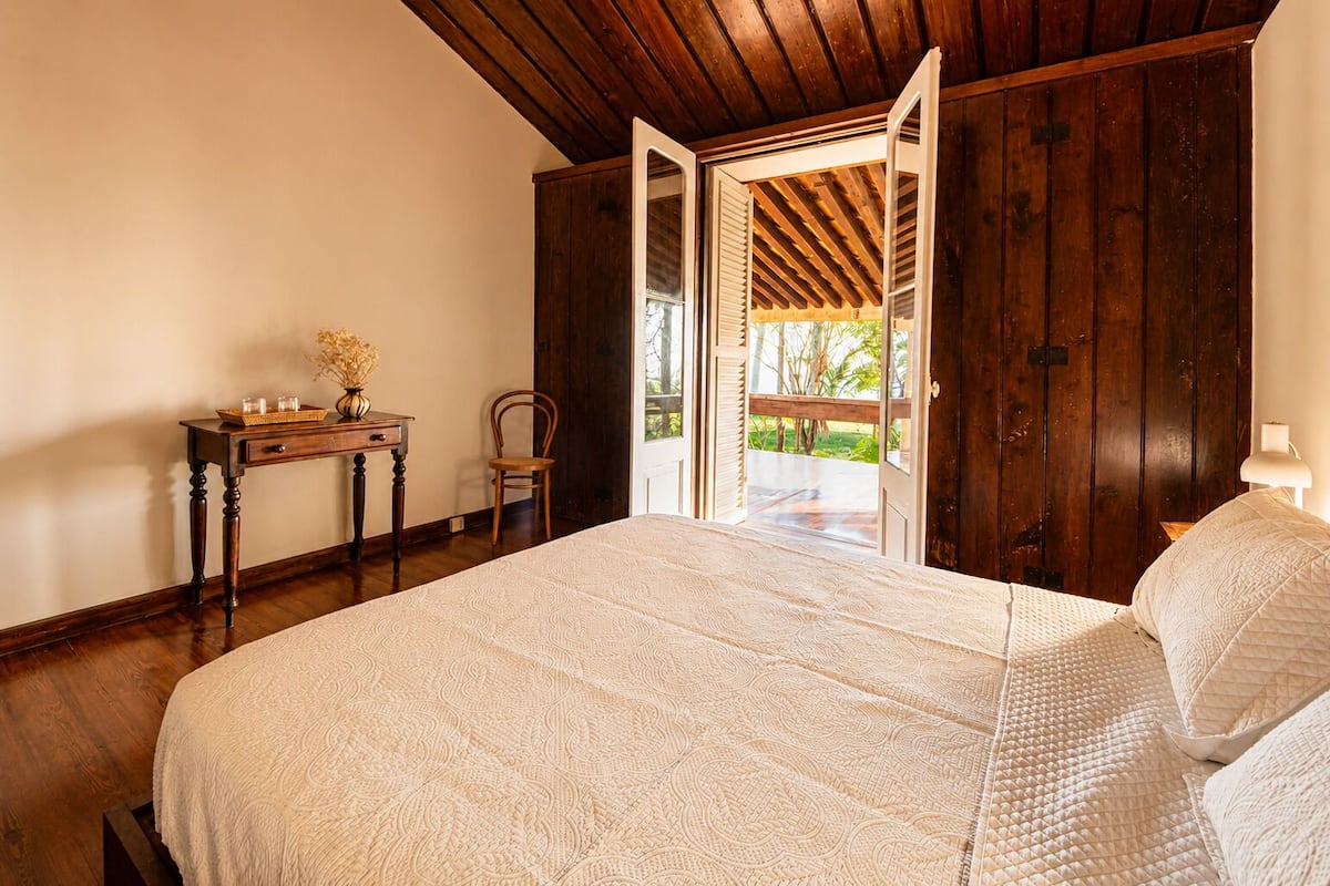 A bedroom with a large bed, wooden furniture, and a view through an open door.