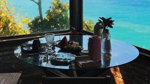 A dining table with a view of the ocean, a glass vase with a plant, and a bottle of water. -  CLIFFSIDE - Boutique Hotel & Spa (Rio de Janeiro)