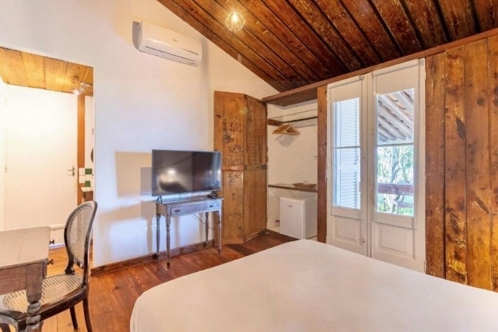 A room with a bed, a television on a stand, a chair, wooden walls, and a door leading to an outdoor area.