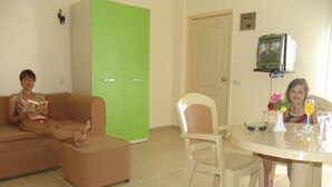 A living room with a sofa, a chair, a table with a vase and glasses, and a television on a stand. - Hotel Olivia (Kusadasi)