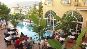 A rooftop pool area with tables and chairs, surrounded by large windows and tropical plants. - Hotel Olivia (Kusadasi)