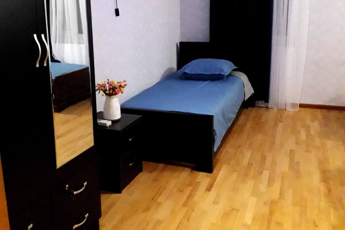 A bedroom with a bed, a dresser, a nightstand, a mirror, and a wall-mounted light fixture.