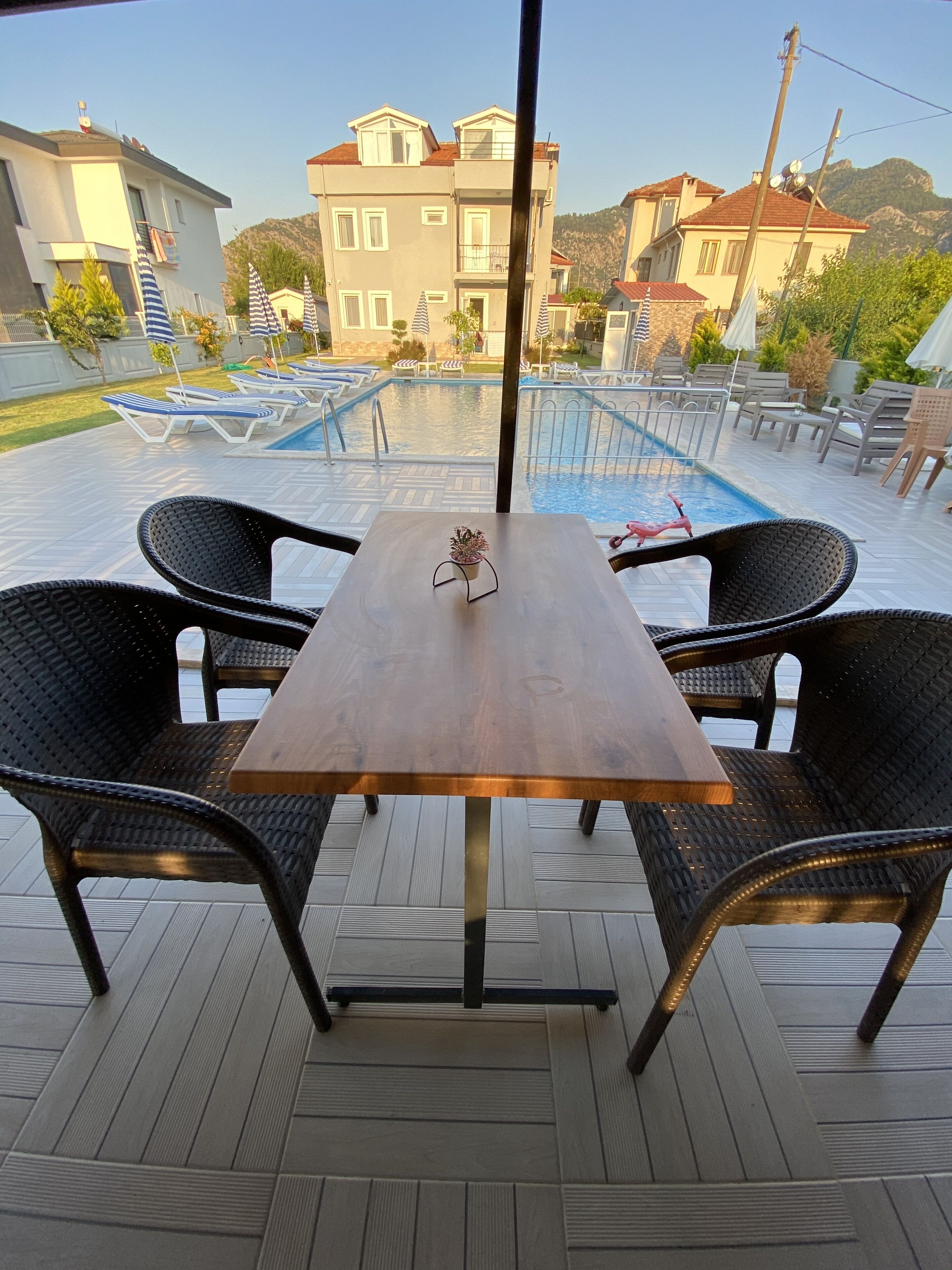 Un espace aménagé au bord de la piscine, avec une table et des chaises, une piscine, et des bâtiments en arrière-plan.