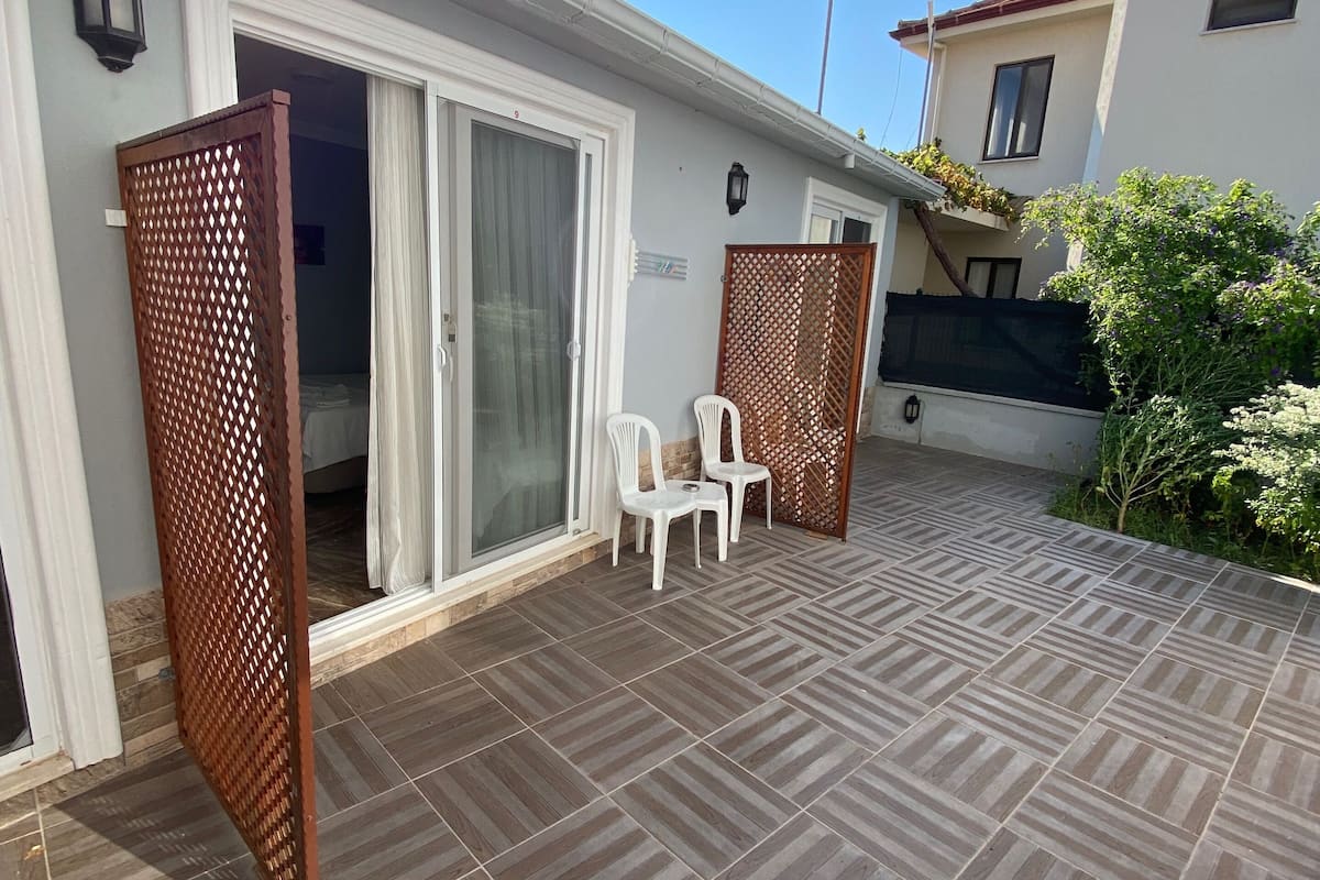 A patio with patterned tiles, a sliding glass door, and two white plastic chairs.