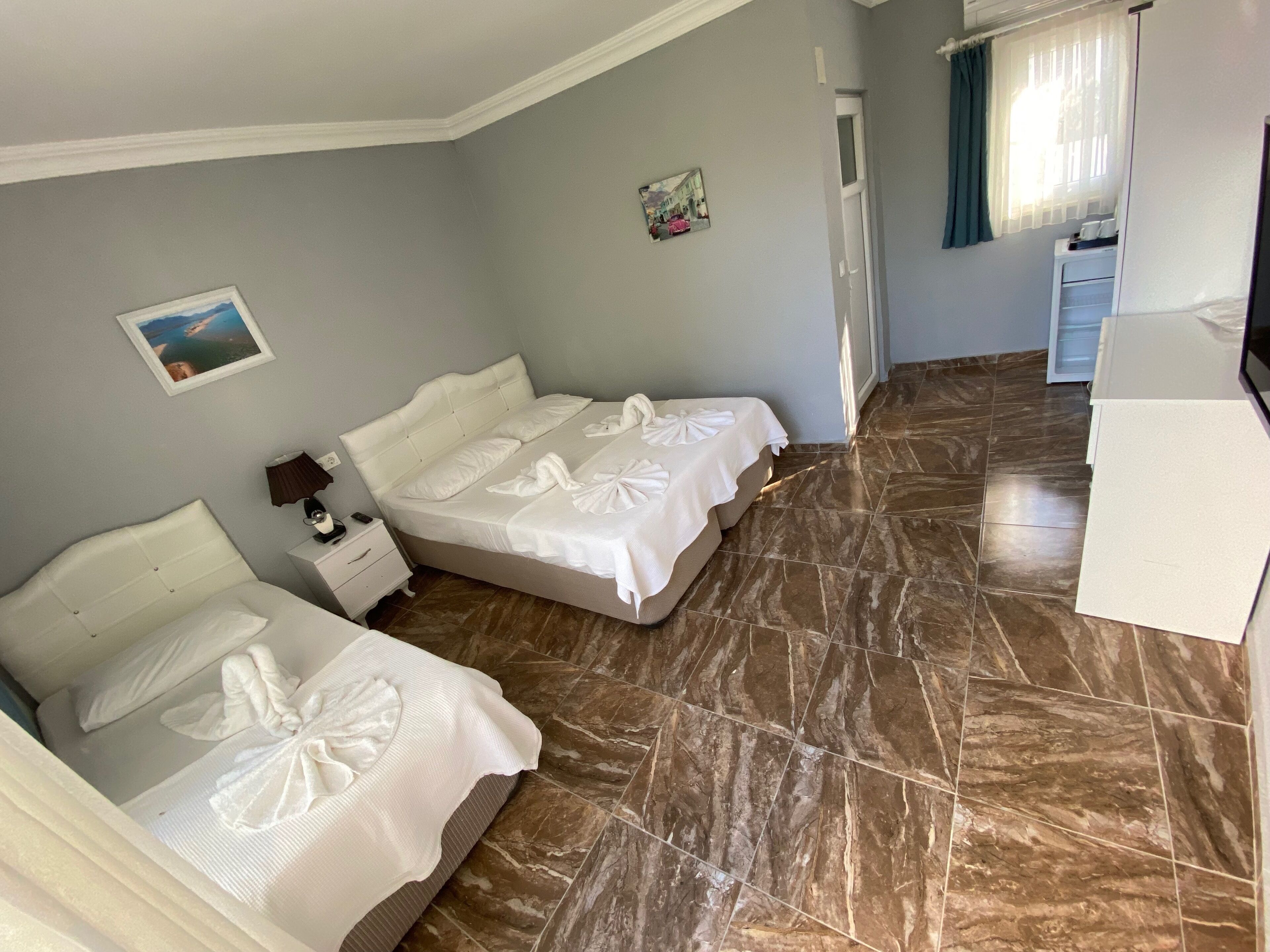 A hotel room with two beds, a small bedside table with a lamp, a picture on the wall, and a view of the hallway.