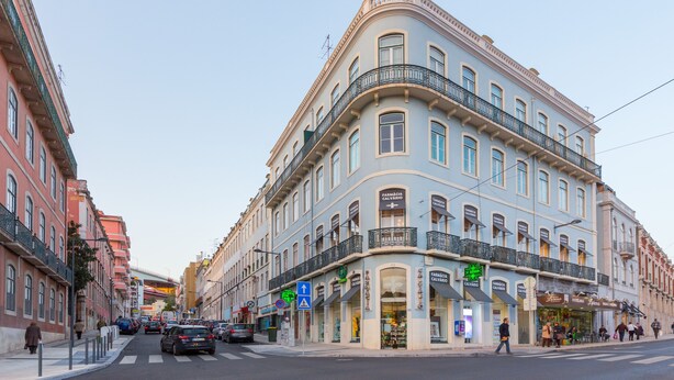 Un immeuble à plusieurs étages, avec une entrée d’angle, des devantures de magasins et une façade donnant sur la rue.