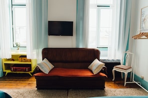 Uma sala de estar com um sofá marrom, uma televisão na parede e uma pequena mesa com uma planta.