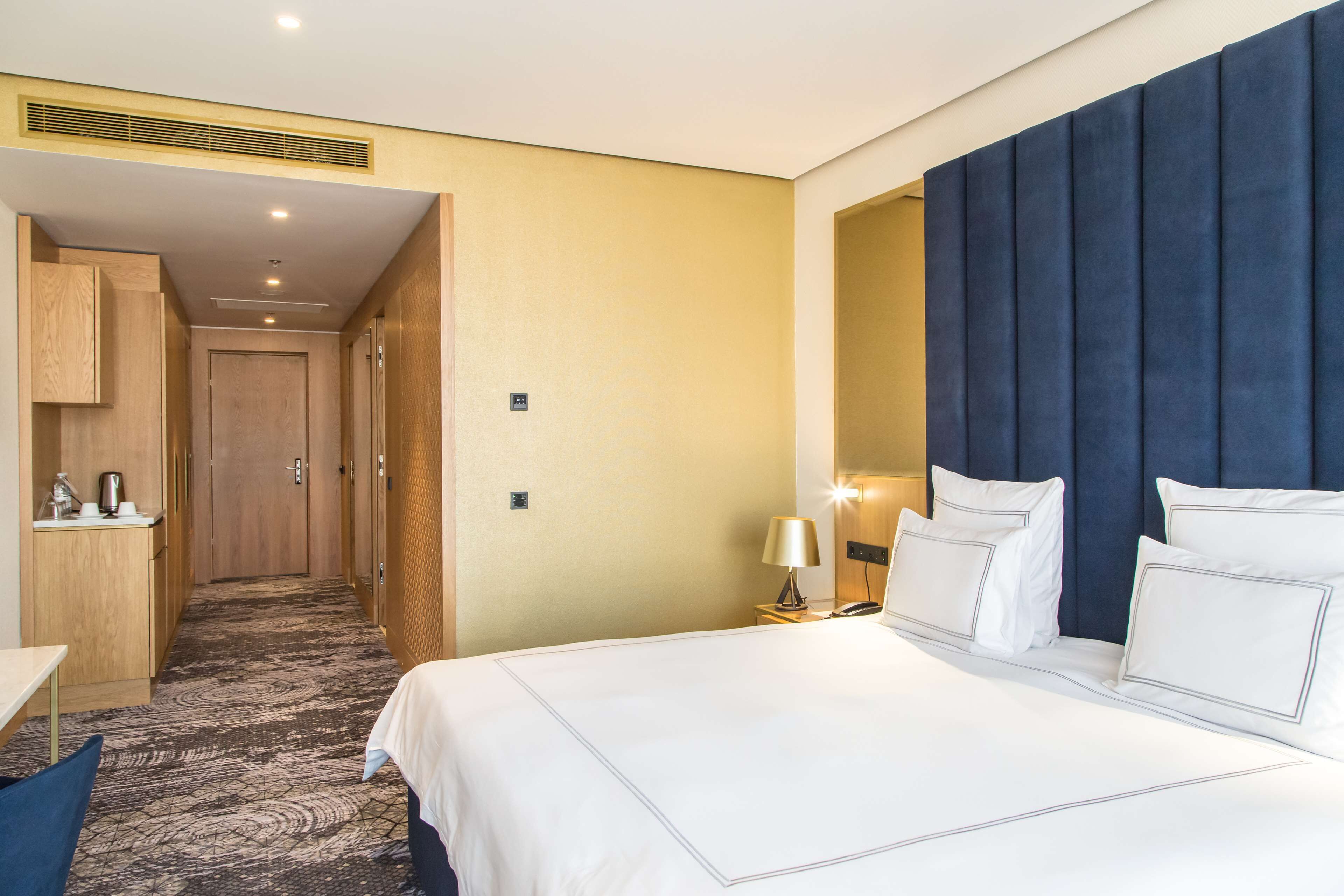 A hotel room with a large bed, a desk, a chair, a wardrobe, and a bathroom.