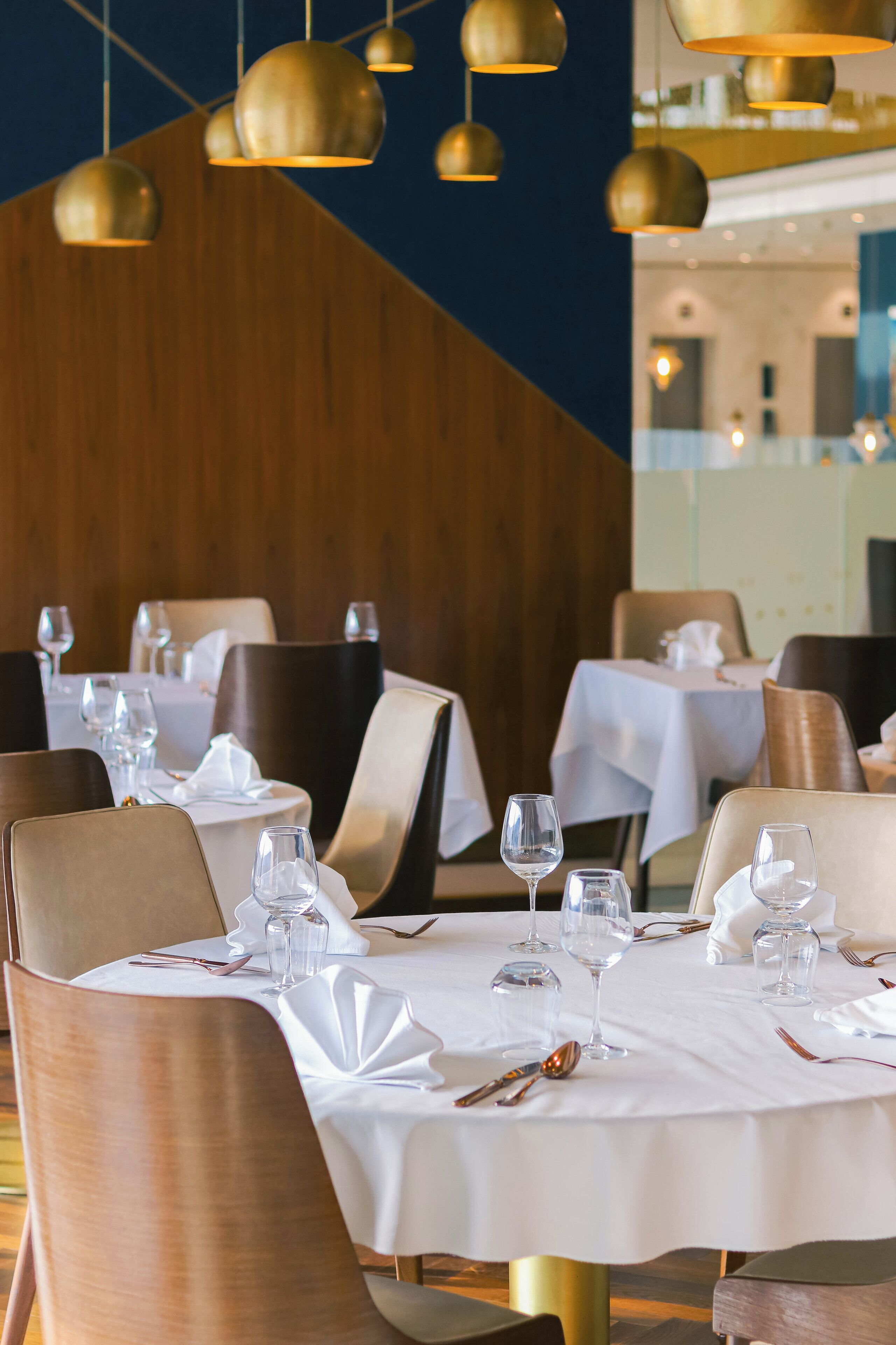 Un restaurante con mesas redondas cubiertas con manteles blancos, sillas doradas y lámparas colgantes de oro.