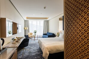A hotel room with a bed, a desk with a chair, a small table with a lamp, and a sofa. - Swissotel Sarajevo (Sarajevo)