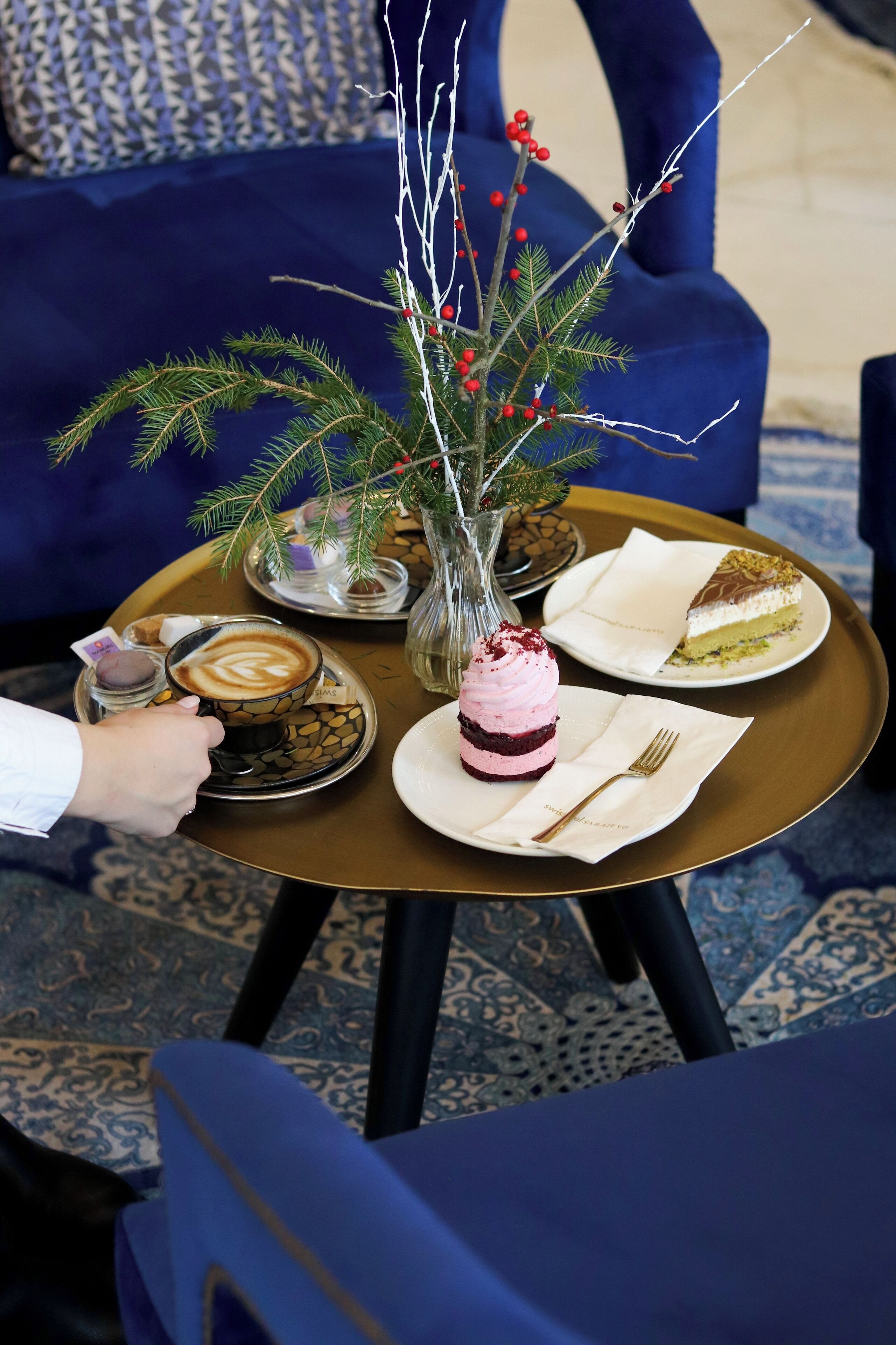 A dining table with a coffee cup, a dessert, and a vase with branches and berries.