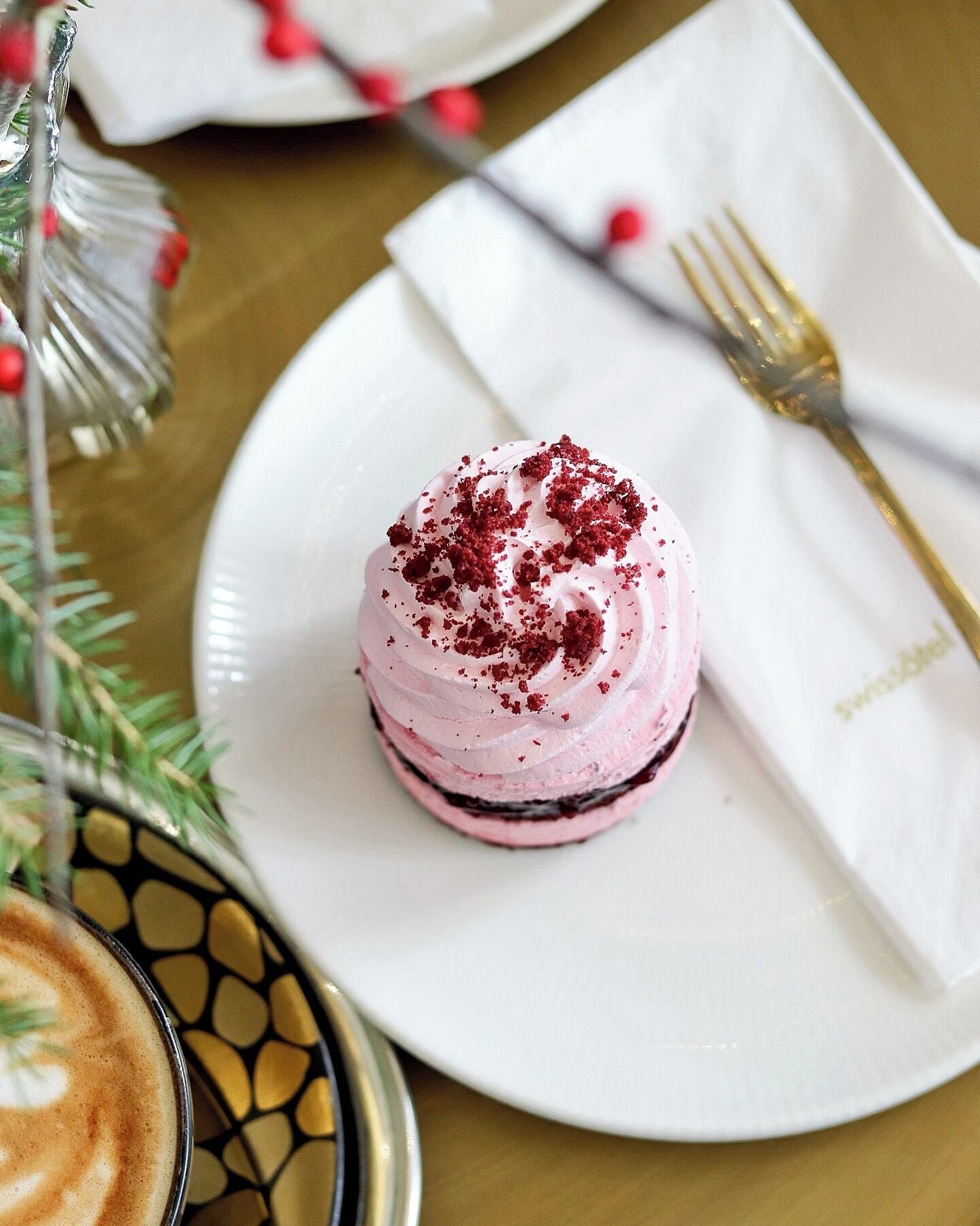 A dessert on a white plate with a gold fork and napkin, a glass of coffee, and a Christmas tree in the background.