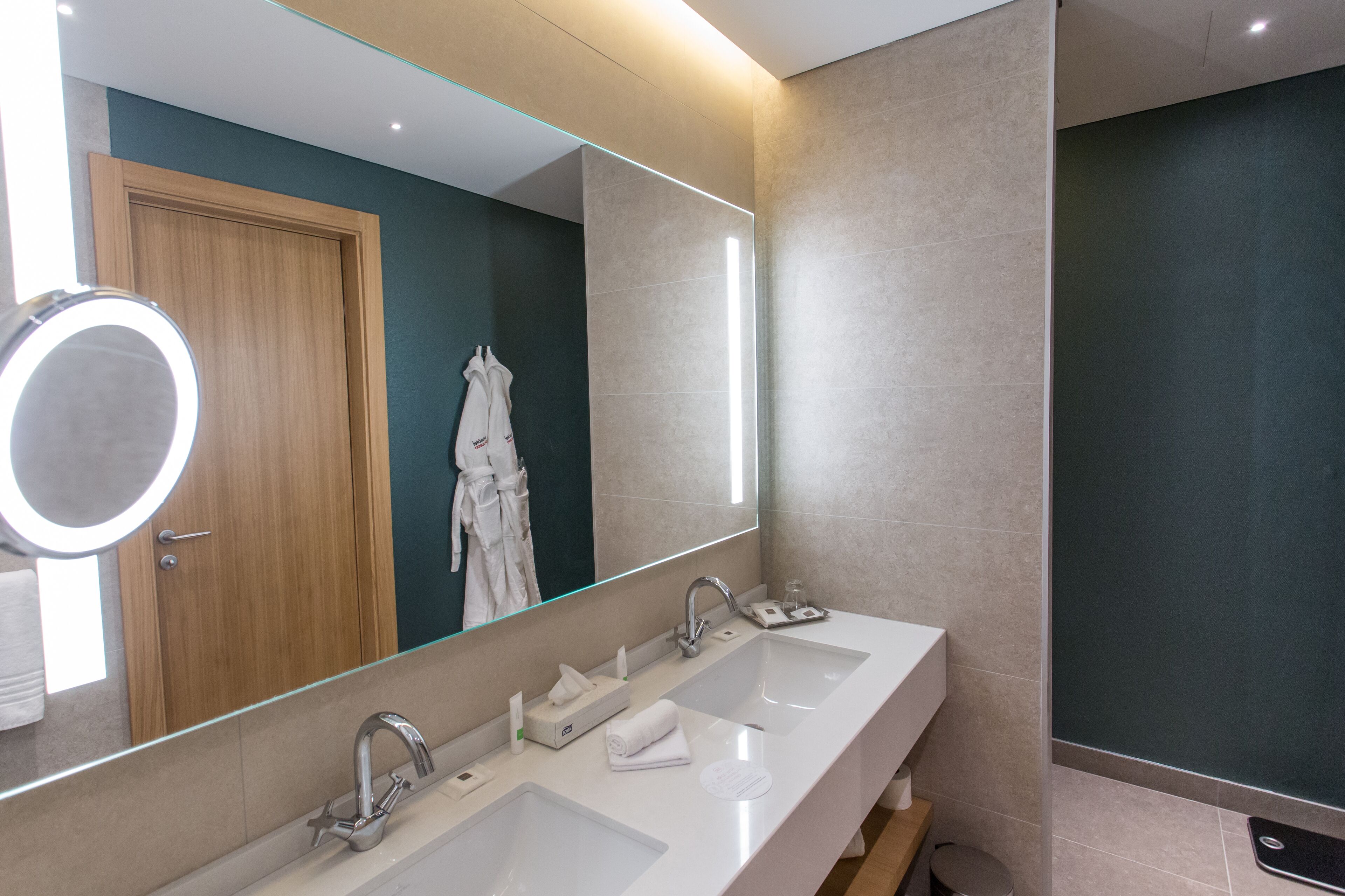 A modern bathroom with two sinks, a large mirror, and a robe rack.