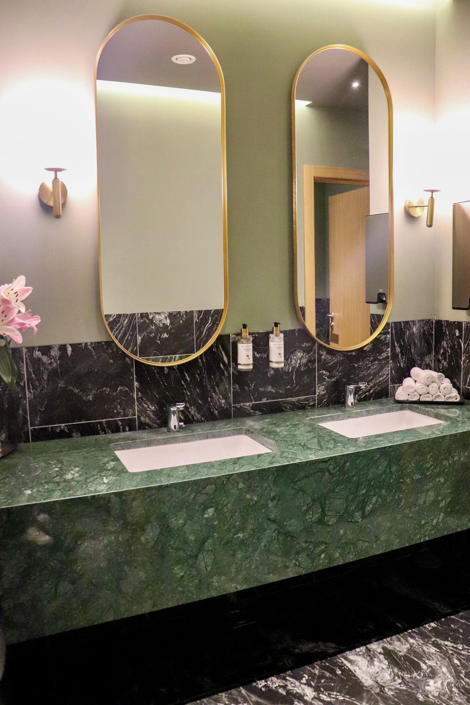 A bathroom with two sinks, marble countertops, and large mirrors with gold frames.