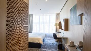 A hotel room with a bed, desk, and a large window with curtains.