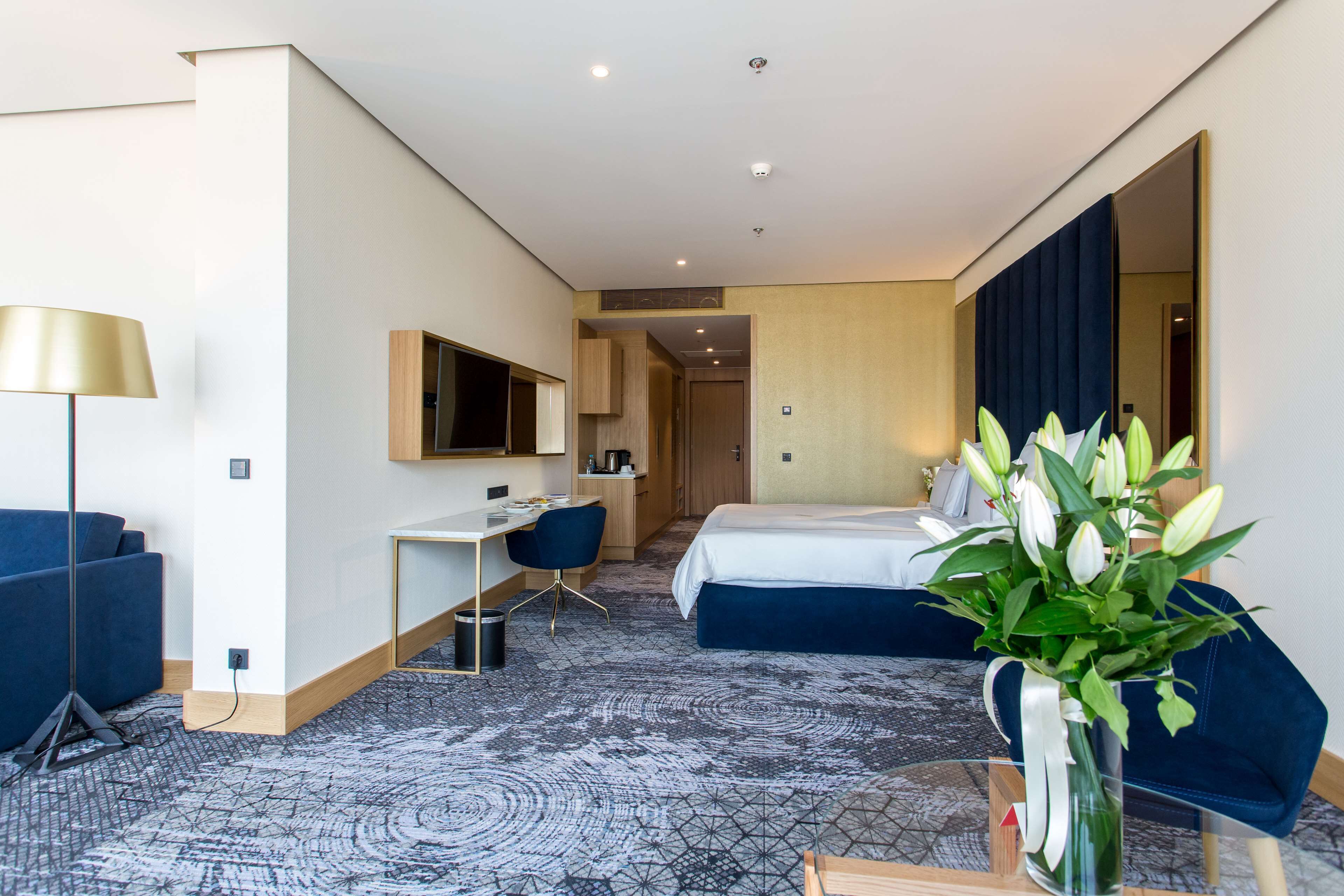 A hotel room with a bed, desk, chair, and a vase of flowers.