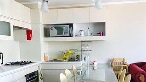 A modern kitchen with a glass dining table, white cabinets, and a red sofa. - Departamento Algarrobo Condominio Laguna (Algarrobo)