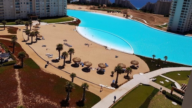 A resort with a large pool, palm trees, and a view of the ocean. - Departamento Algarrobo Condominio Laguna (Algarrobo)