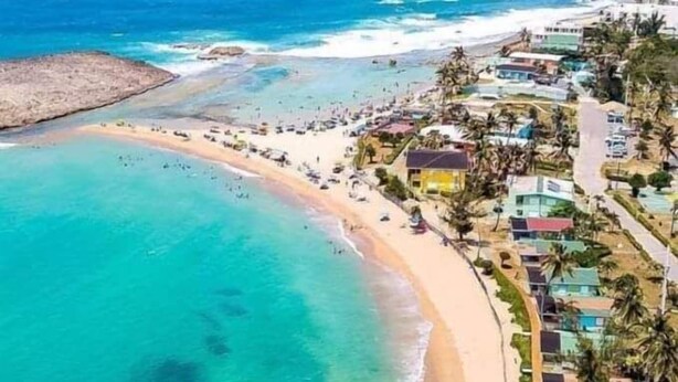 An aerial view of a coastal area with a beach, clear blue waters, and buildings along the shore. - Colinas del Atlantico Vacational House 2nd Floor (Isabela)