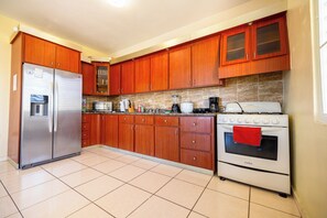 A kitchen with wooden cabinets, a stainless steel refrigerator, a stove, and various appliances. - Colinas del Atlantico Vacational House 2nd Floor (Isabela)