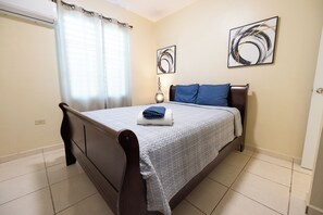 A bedroom with a bed, curtains, a bedside table, and two wall art pieces. - Colinas del Atlantico Vacational House 2nd Floor (Isabela)