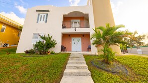 A two-story building with a central entrance, a balcony on the upper floor, and a small garden area with a palm tree. - Colinas del Atlantico Vacational House 2nd Floor (Isabela)