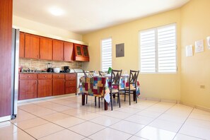A kitchen with wooden cabinets, a dining table with chairs, and a tiled floor. - Colinas del Atlantico Vacational House 2nd Floor (Isabela)