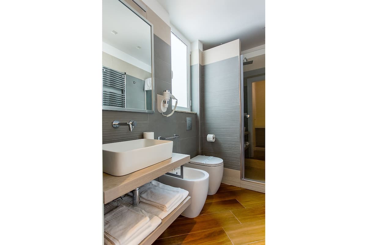 A modern bathroom with a large mirror, a vessel sink, a toilet, and a shower area.