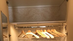 A walk-in closet with a mirrored closet door, a hanging rod with wooden hangers, and a patterned wallpaper. - NovaNova (Naples)