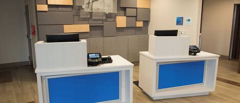 Two reception desks with digital kiosks, a modern wall design, and a clean floor.