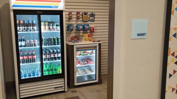 A vending machine with various beverages and snacks, a small refrigerator with frozen items, and a sign indicating a market area.