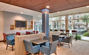 A modern indoor seating area with tables and chairs, a large pillar, and a television screen on the wall. - Holiday Inn Express & Suites Gainesville I-75 by IHG (Gainesville)