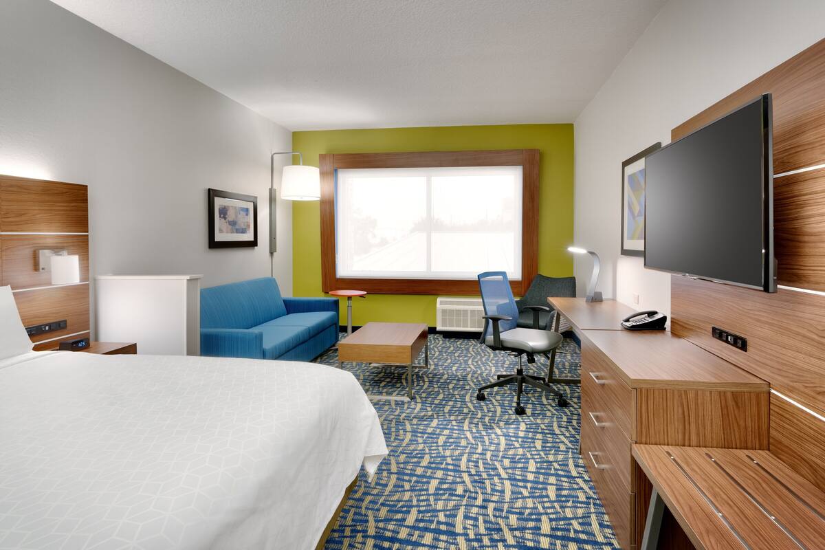 A hotel room with a bed, a desk, a chair, a TV, and a window.