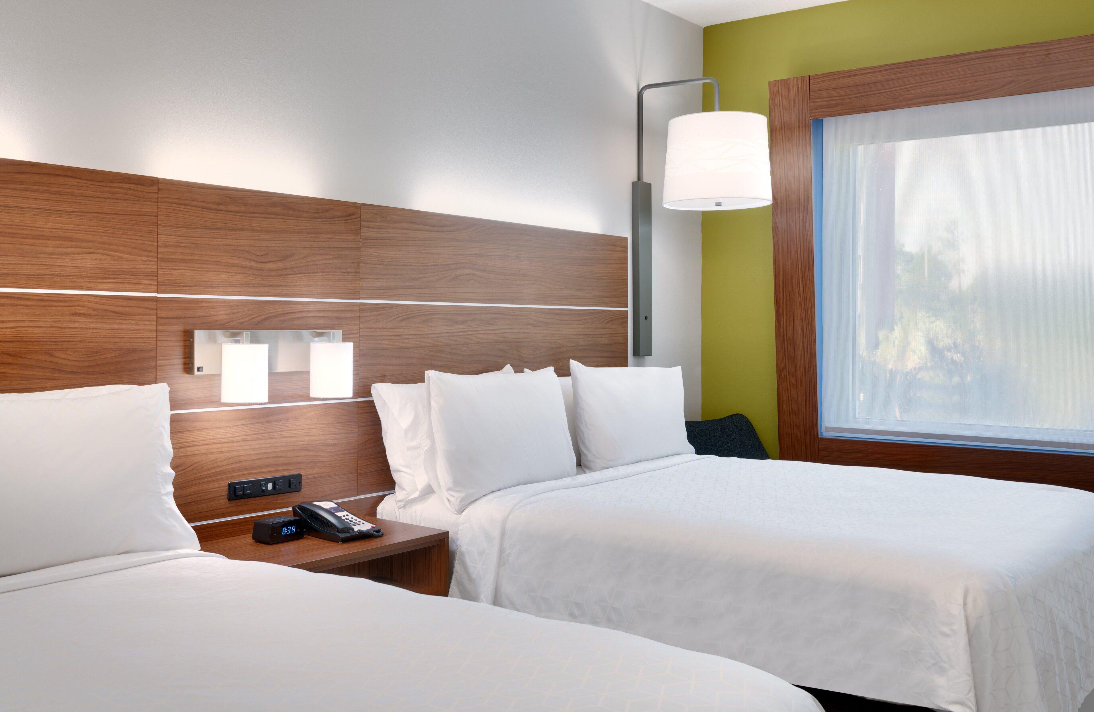 Ein Hotelzimmer mit zwei Betten, einem Nachttisch mit Telefon, einer Wandlampe und einem Fenster mit Blick.