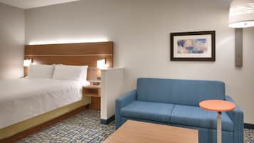 A hotel room with a bed, a nightstand, a blue sofa, a small table, and a framed picture on the wall.