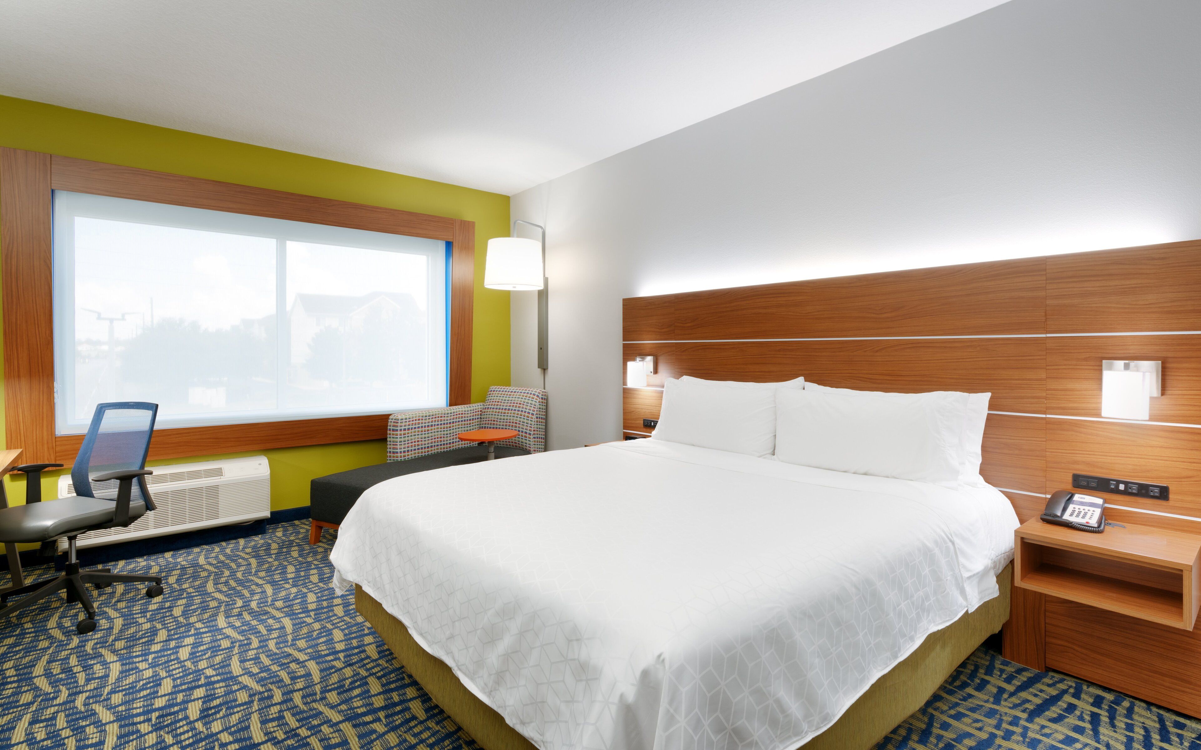 Habitación de hotel con una cama grande, un escritorio con silla, ventanal con vista y mesita de noche con teléfono.
