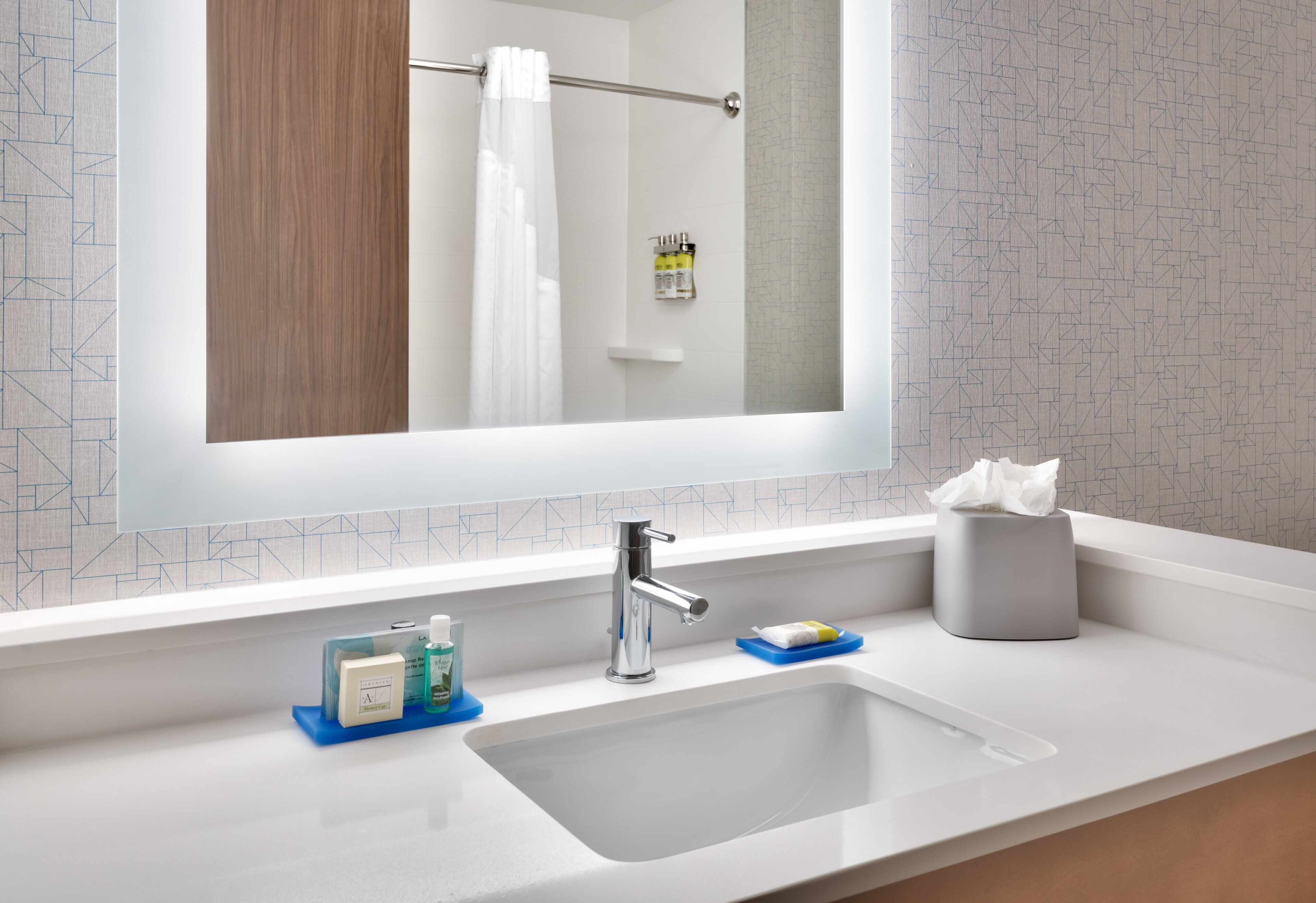Une salle de bain moderne avec un grand miroir, un lavabo, un porte-serviettes et un boîte à mouchoirs.