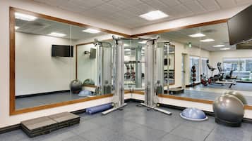 Uma academia com equipamentos de exercício, um espelho e uma janela.