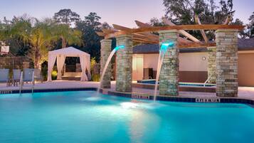 A swimming pool with a waterfall feature, a covered seating area, and a clock on the wall.