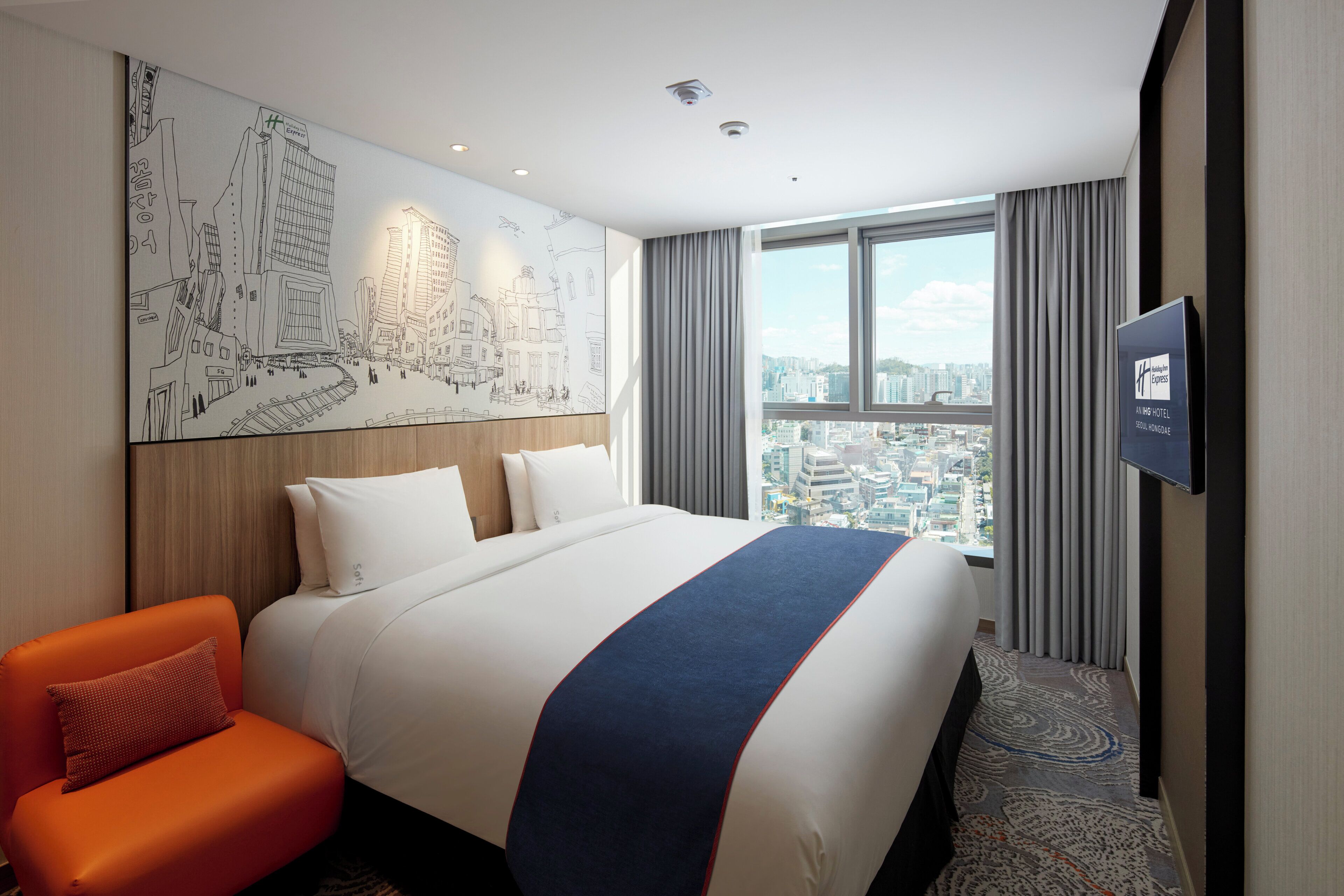 Habitación de hotel con una cama grande, vista panorámica de la ciudad, televisor montado y un cuadro con un paisaje urbano.